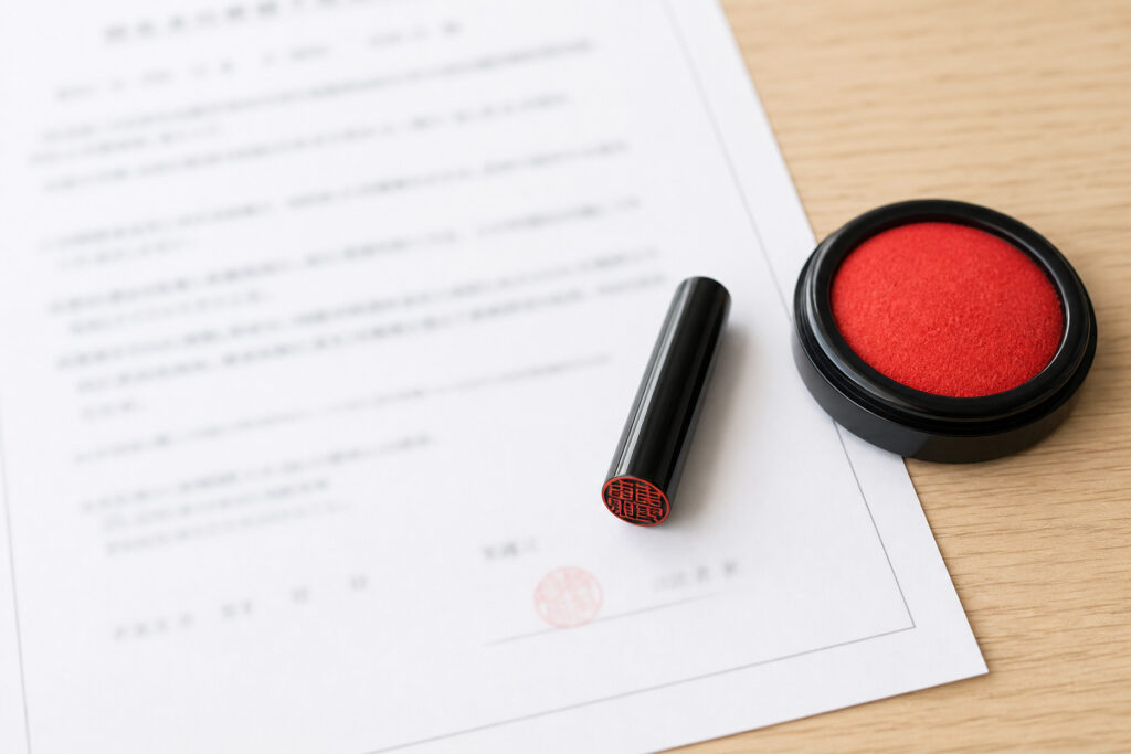 木目調のデスク上に置かれた契約書類と印鑑・朱肉を示す、不動産取引や注文住宅の建築契約・名義変更手続きをイメージした写真。